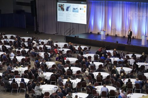 conference in large room with people at tables listening to speaker